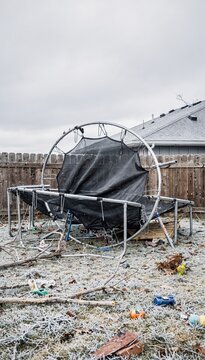 Damaged trampoline flipped over in residential backyard after severe wind storm for insurance claim documentation with debris on grass and a cloudy sky background