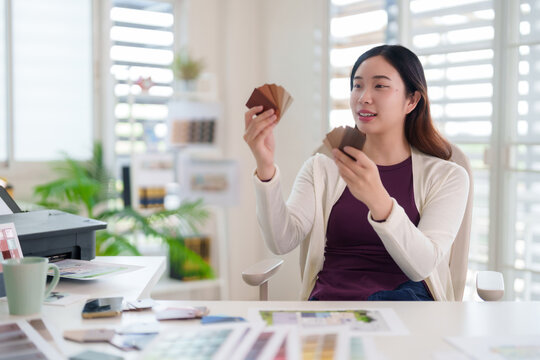 Adult Asian female designer examining material swatches office creative interior architect selecting design options planning project development