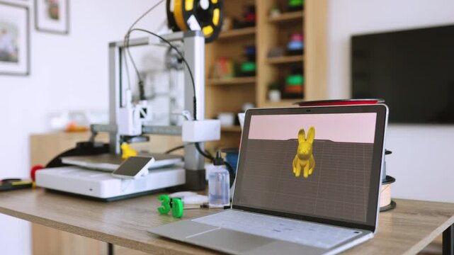 A laptop displays a 3D model next to a 3D printer and filament spools, showcasing a creative manufacturing process