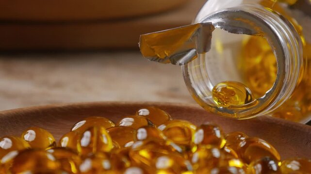 softgel capsules pouring out of opened glass bottle onto wooden plate, supplement herbal extract health concept