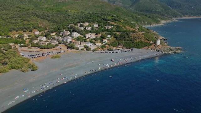 Drone aerial view of Plage d'Albo beach with swimmers and umbrellas near the historic Genoese tower in the coastal village of Albo, Cap Corse, Corsica, France. Scenic Mediterranean shoreline with dark