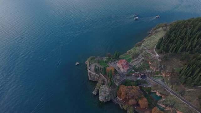 Panoramic drone descent over the Church of Saint John at Kaneo, revealing the rooftops of Ohrid city and the scenic Lake Ohrid landscape in the background.