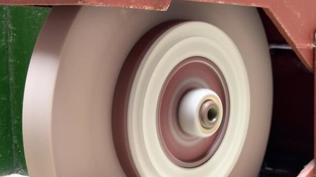 A motorized abrasive wheel rotates at high speed against its housing. The rapid motion generates a consistent, mechanical whirring sound and a low-frequency hum.