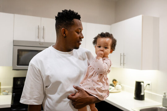Father holding baby daughter smiling and bonding at home, multiracial family