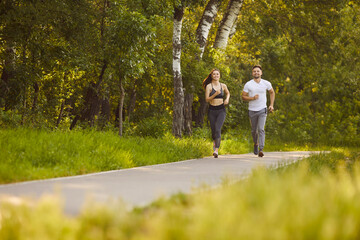 Obraz premium Morning healthy run of happy couple in summer park, fit man and woman training outdoors. Friends athletes or husband and wife running together to enjoy nature and time together. Workout, life concept