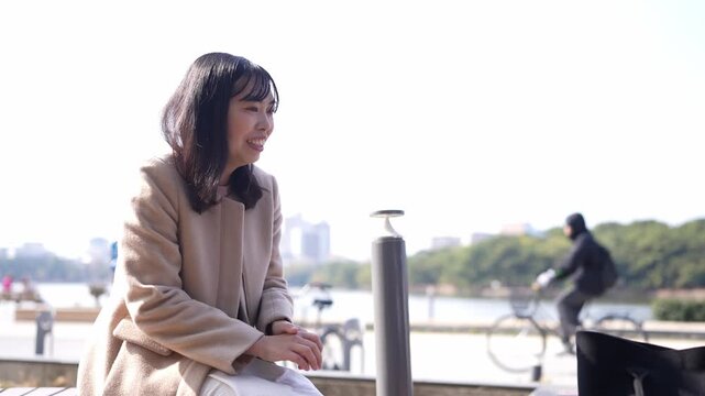 Soft light glows on a woman's thoughtful face. She gazes across a calm waterway, hands resting gently. Her coat frames quiet contemplation against a distant cityscape. Perfect for scenes of pause