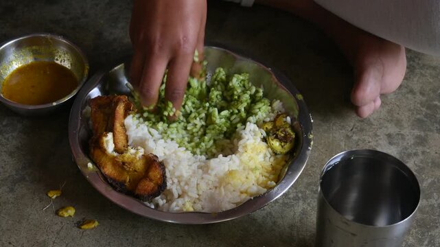 A person is eating piping hot white rice and fish curry. It is served alongside fried fish and roasted bitter gourd. Homemade, traditional Indian food. Indian meal, served in a traditional steel plate