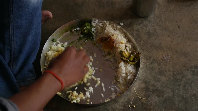 A person is eating piping hot white rice and fish curry. It is served alongside fried fish and roasted bitter gourd. Homemade, traditional Indian food. Indian meal, served in a traditional steel plate