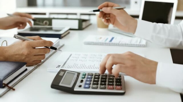 Close up of hands calculating figures and writing on documents
