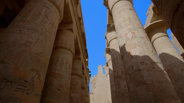 Karnak Temple in Luxor, Egypt. Towering hieroglyphic columns with original red pigment in Great Hypostyle Hall, Karnak Temple Luxor Egypt. Dramatic upward view against vivid blue sky