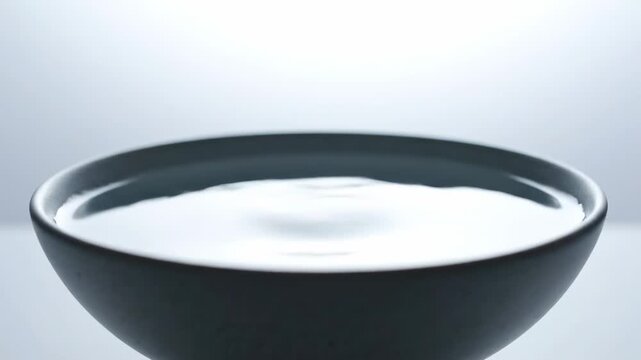 Water droplet falls into a black bowl, creating ripples on the surface, captured in a series of frames showcasing the continuous action and fluid dynamics