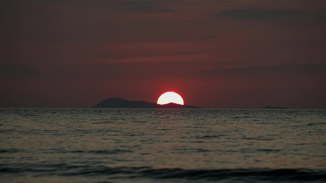 Sunset with half big red sun over the sea and island