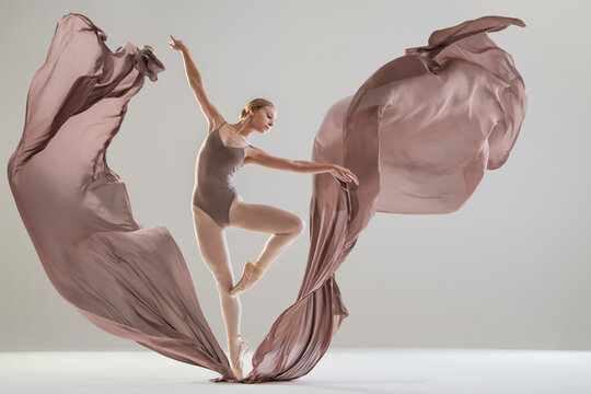 Young ballerina dancing with flowing beige fabric