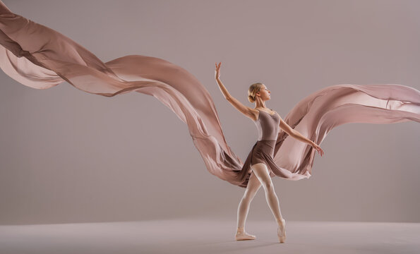 Young ballerina girl in pointe dancing with developing beige fabric