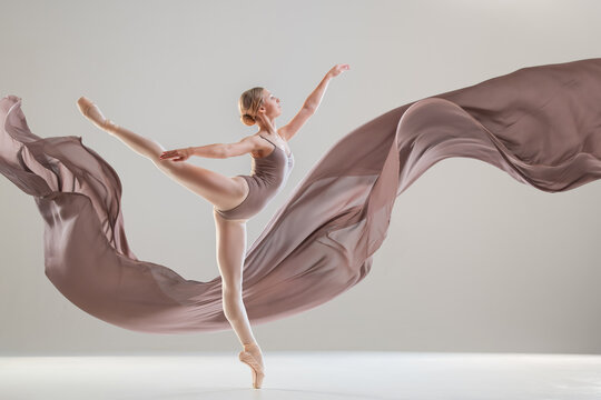 Young ballerina in pointe shoes dancing with developing beige fabric