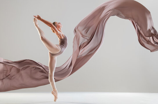 Young ballerina dancing with flowing beige fabric in motion