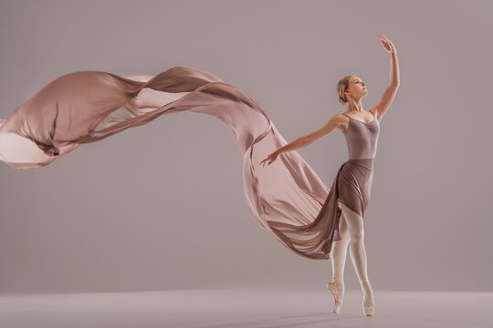 Young ballerina posing with flowing beige fabric in studio