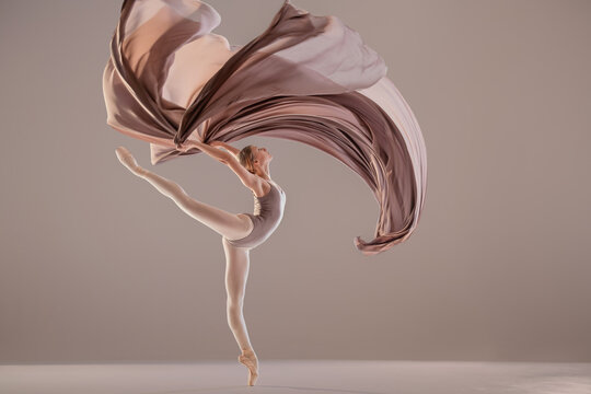 ballerina performing high leg extension with flowing beige fabric
