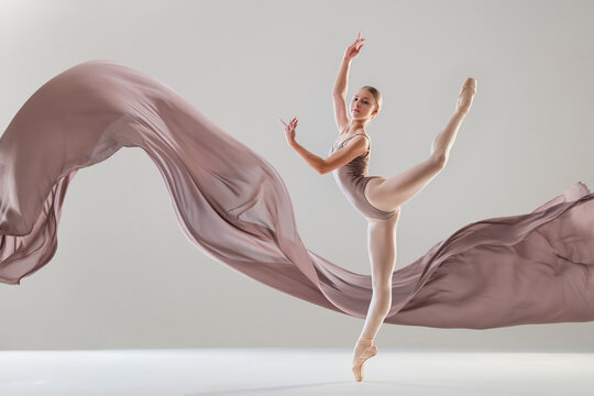 Young ballerina dancing with developing beige fabric