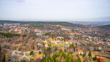 Fototapeta premium A wide view of a small town surrounded by trees and hills. Several buildings are visible, with roads and cars parked nearby. The scene shows a clear sky above.