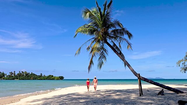 Two visitors walk along the soft sands of Koh Kood Island Thailand, framed by swaying palms and sparkling blue waters. relaxation and exploration of this tropical paradise.