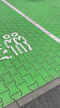 Angled closeup of green parking bays showing white car icon on painted tiles. Designated parking area for car sharing vehicles, supporting urban mobility and convenient short-term transport solutions.