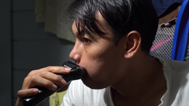 Asian man meticulously shaving his mustache using a modern electric shaver. Close-up profile shot showing facial grooming routine, skin care, and personal hygiene in a domestic setting. High-quality 4
