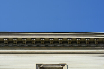 Ornate architectural cornice featuring decorative dentil molding and horizontal stone lines against a clear and cloudless blue sky © nahhan