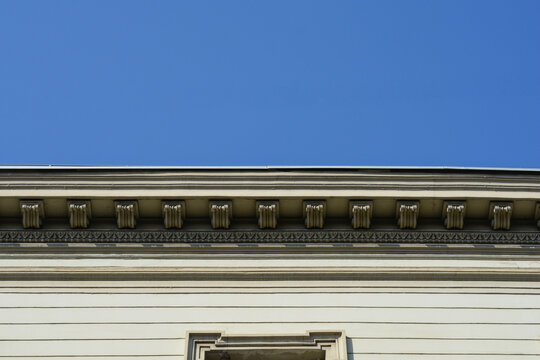 Ornate architectural cornice featuring decorative dentil molding and horizontal stone lines against a clear and cloudless blue sky