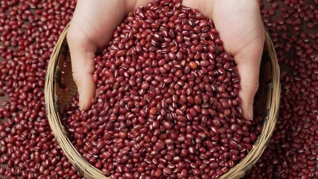 Hands scooping and holding adzuki beans from a traditional bamboo basket