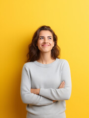 Fototapeta premium Smiling young woman looking up with folded arms against a bright yellow background.