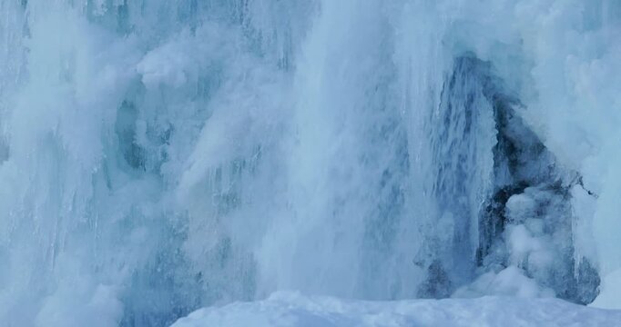Stunning close-up view of a massive frozen waterfall creating dramatic ice formations in Iceland winter landscape. Brilliant blue glacial ice textures cascade down rocky cliff face with intricate