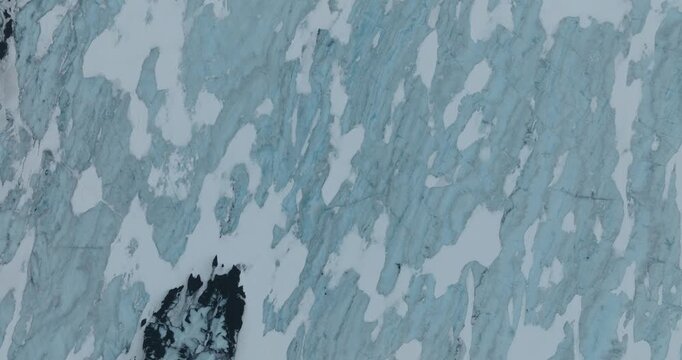 Stunning overhead drone footage reveals hikers trekking through intricate patterns of glacial ice and snow formations with deep blue crevasses and Icelandic tundra