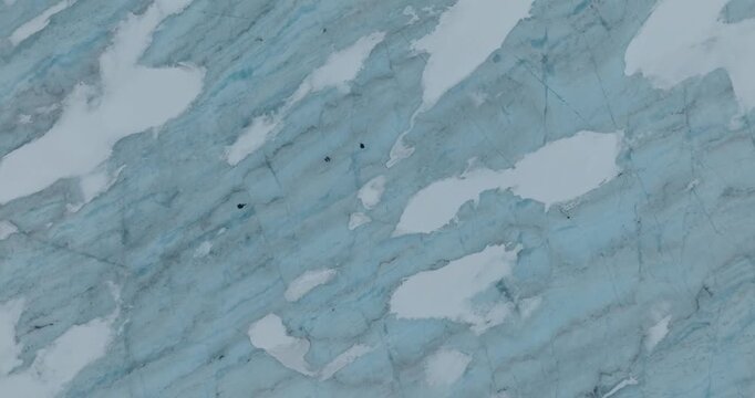 Stunning overhead drone footage captures Arctic sea ice formations with intricate patterns of frozen blue and white glacial textures. Hikers cross the ice far below