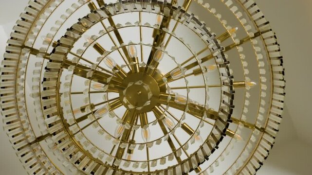 A low angle view looking directly up at a luxurious golden tiered chandelier with crystal elements and warm light bulbs hanging from a white ceiling