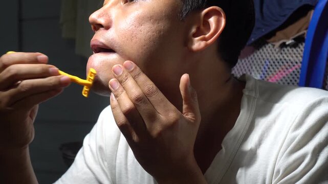 Detailed shot of a young man shaving his beard with a yellow disposable razor. Focusing on male grooming, skincare, and daily hygiene routine. Highlighting skin texture and the process of self-care fo