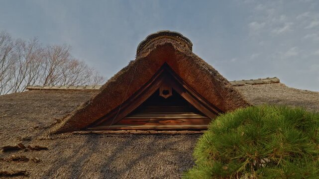 A detailed shot of a historic minka house's thatched roof, showing the triangular gable and wooden ventilation structure against a clear sky.