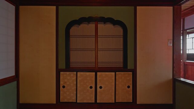 A symmetrical shot of a traditional Japanese study area featuring a decorative shoji screen with a curved top and patterned sliding doors on a lower cabinet (Jibukuro).