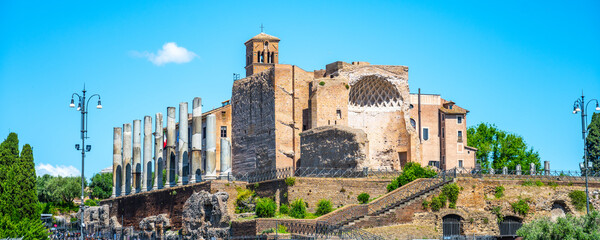 Naklejka premium Tourists walk around the Temple of Venus and Roma, located in the east part of the Roman Forum. This site shows the remains of ancient architecture and historic pillars.