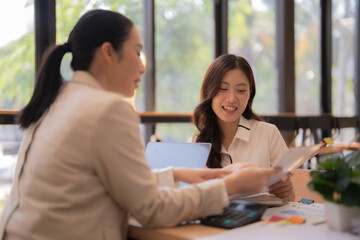Obraz premium Two professional Asian women discussing documents and business strategy during a collaborative meeting in a modern office, focusing on teamwork and partnership