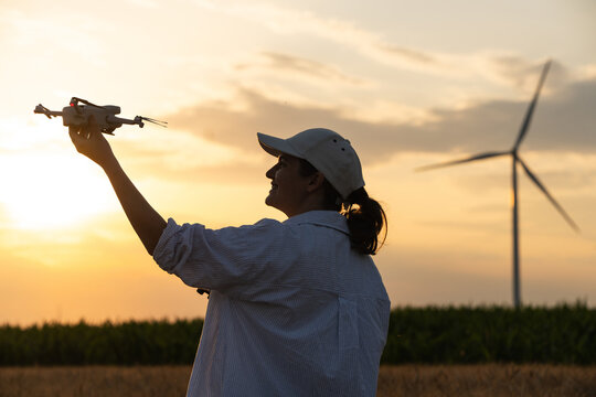 Farmer using drone for smart farming with wind turbine during sunset