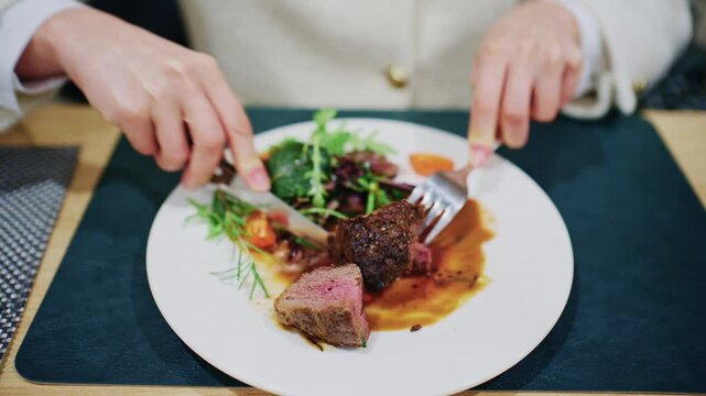 Woman cutting a medium rare steak served with vegetables and sauce on a restaurant plate