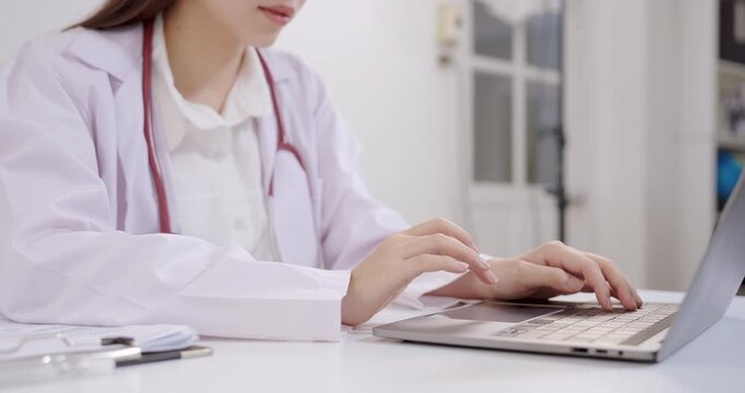 Slowmotion scene of asian female doctor typing on laptop in clinic, healthcare professional performing digital medical record management, representing technology, precision, dedication in healthcare