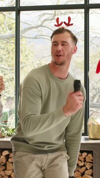 Vertical video: Offering mic, man in green sweater singing holiday song at home with red antlers
