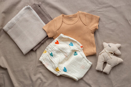 Beige baby bodysuit and white cotton diaper pantie and towels on on beige sheet, top view. Eco friendly cloth and accessories