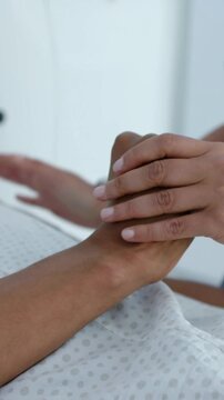 Vertical video: Reaching nurse blue scrubs cupping hand at bedside, comforting with ID band visible