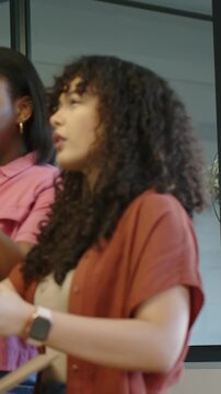 Vertical video: Opening bubblewrap package, woman in pink pointing while peer inspecting at office