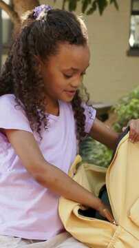 Vertical video: Picking purple pouch girl in tee packing yellow backpack on school bench for class