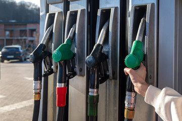 Hand taking fuel nozzle at gas station. Close-up of a person grabbing a green fuel pump nozzle at a gas station, representing refueling, transport, and energy costs. © Iryna