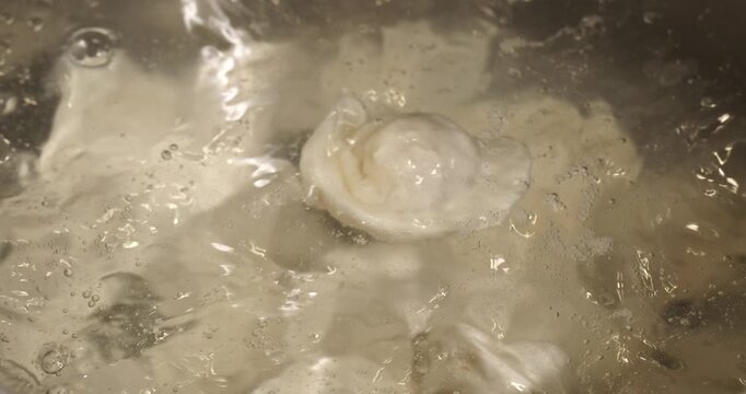 Frozen dumpling being dropped into boiling water, close-up footage. Process of cooking dumplings.